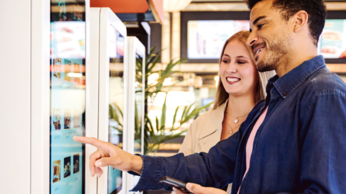 Mann und Frau bedienen lächelnd Self Service Terminal