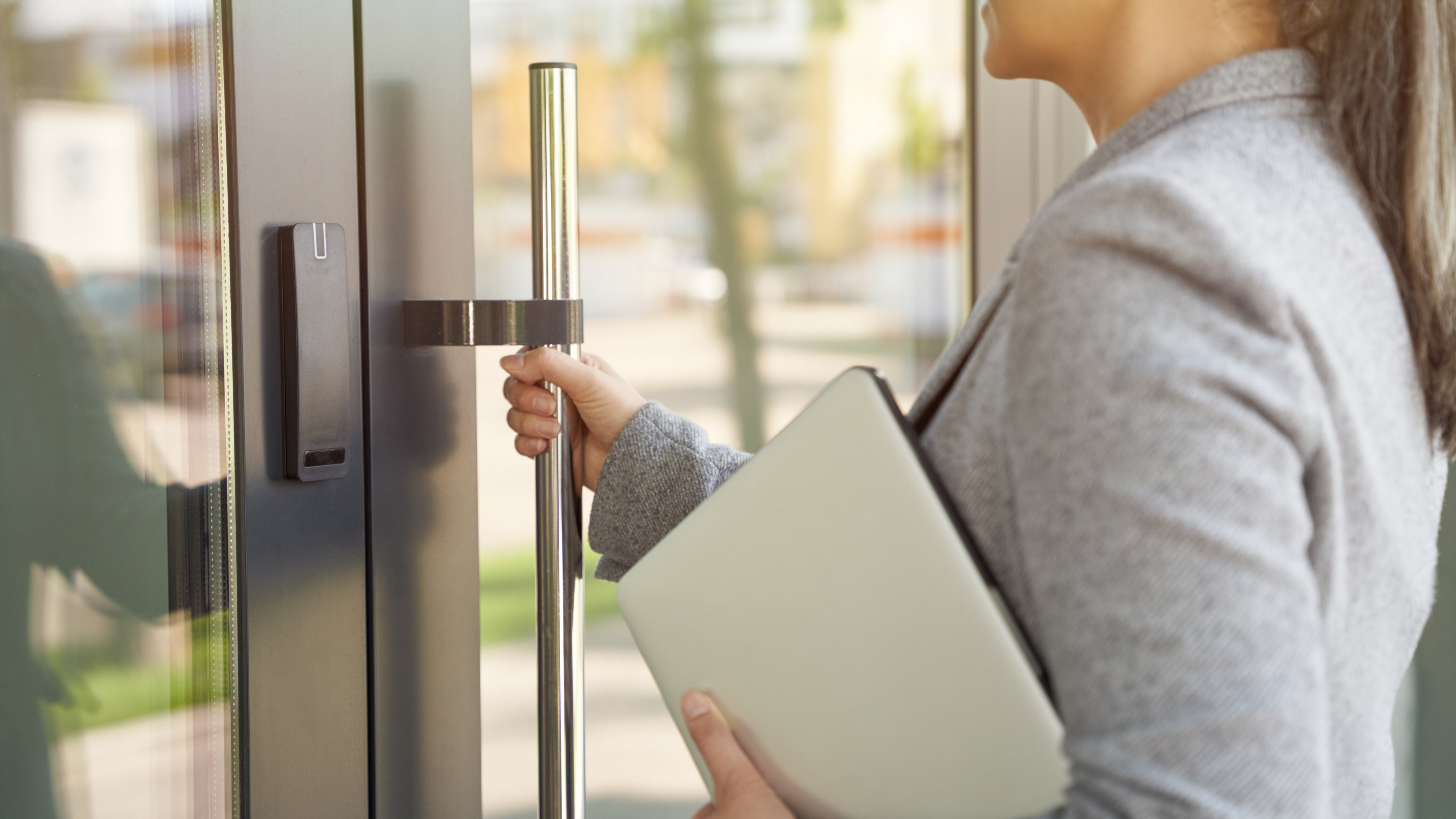 Frau mit Zopf, öffnet Tür und hält dabei einen Laptop im Arm.