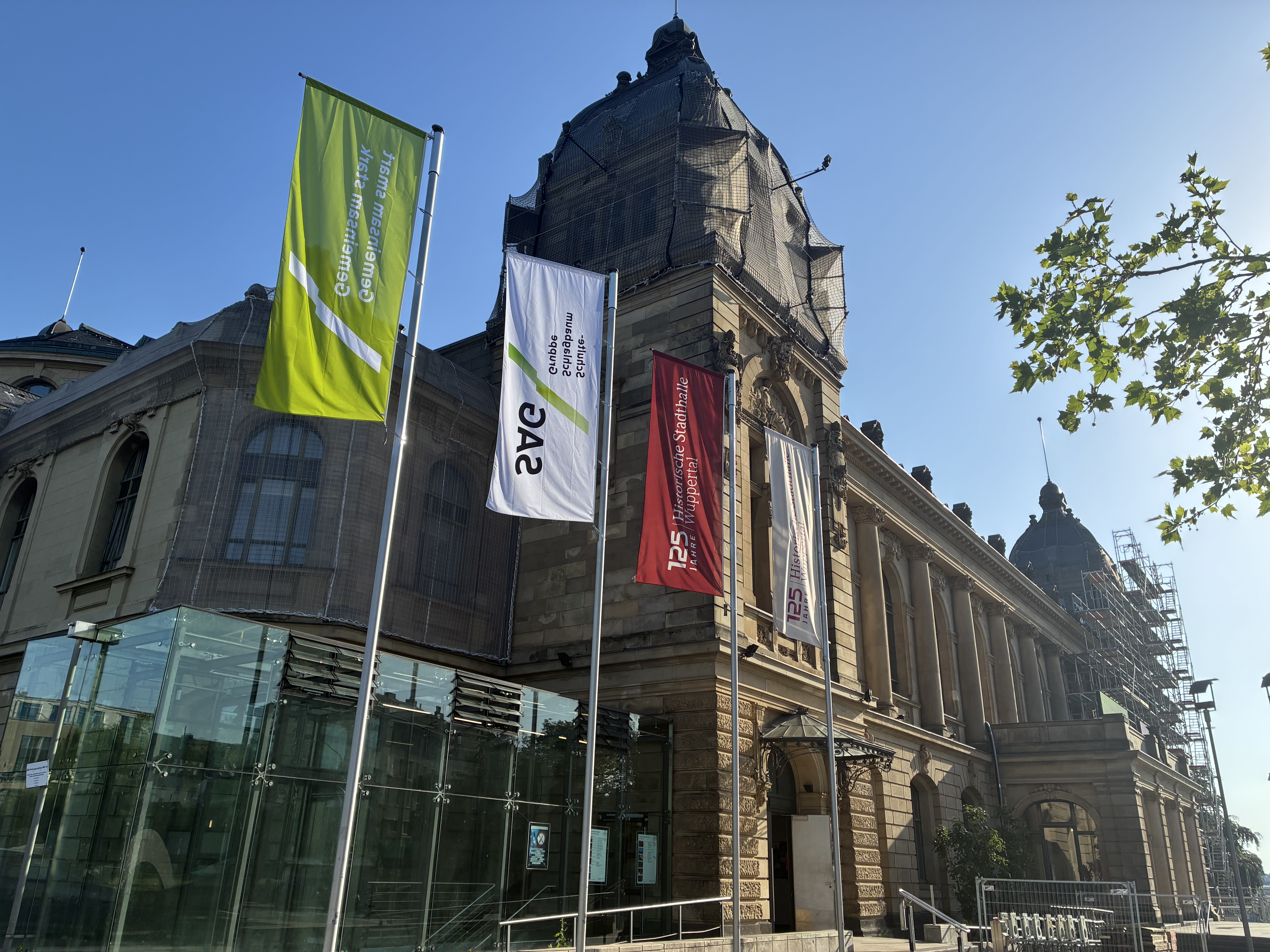 Außenaufnahme Historische Stadthalle Wuppertal, vor dem Gebäude eine weiße und eine grüne Fahne mit dem Logo und Claim der SAG